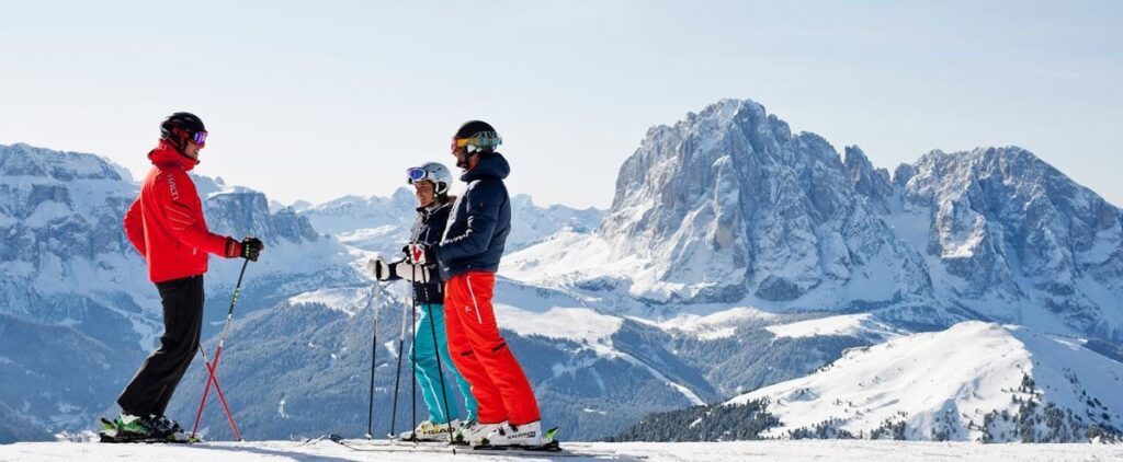 Three friends at the top of a piste in front of mountains